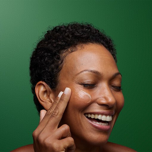 a mature woman smiling while applying a cleansing balm