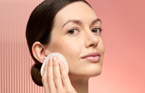 woman using a reusable cotton pad to sweep toner across her face, on a peach background
