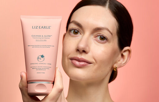 woman holding Cleanse & Glow™ Transforming Gel Cleanser 150ml tube on a peachy background