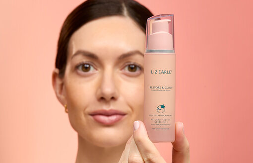 woman holding Restore & Glow™ Instant Radiance Serum 30ml pump on a peach background