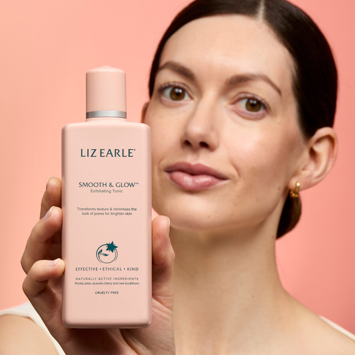 Restore & Glow™ Instant Radiance Serum woman holding Restore & Glow™ Instant Radiance Serum 30ml pump on a peach background
