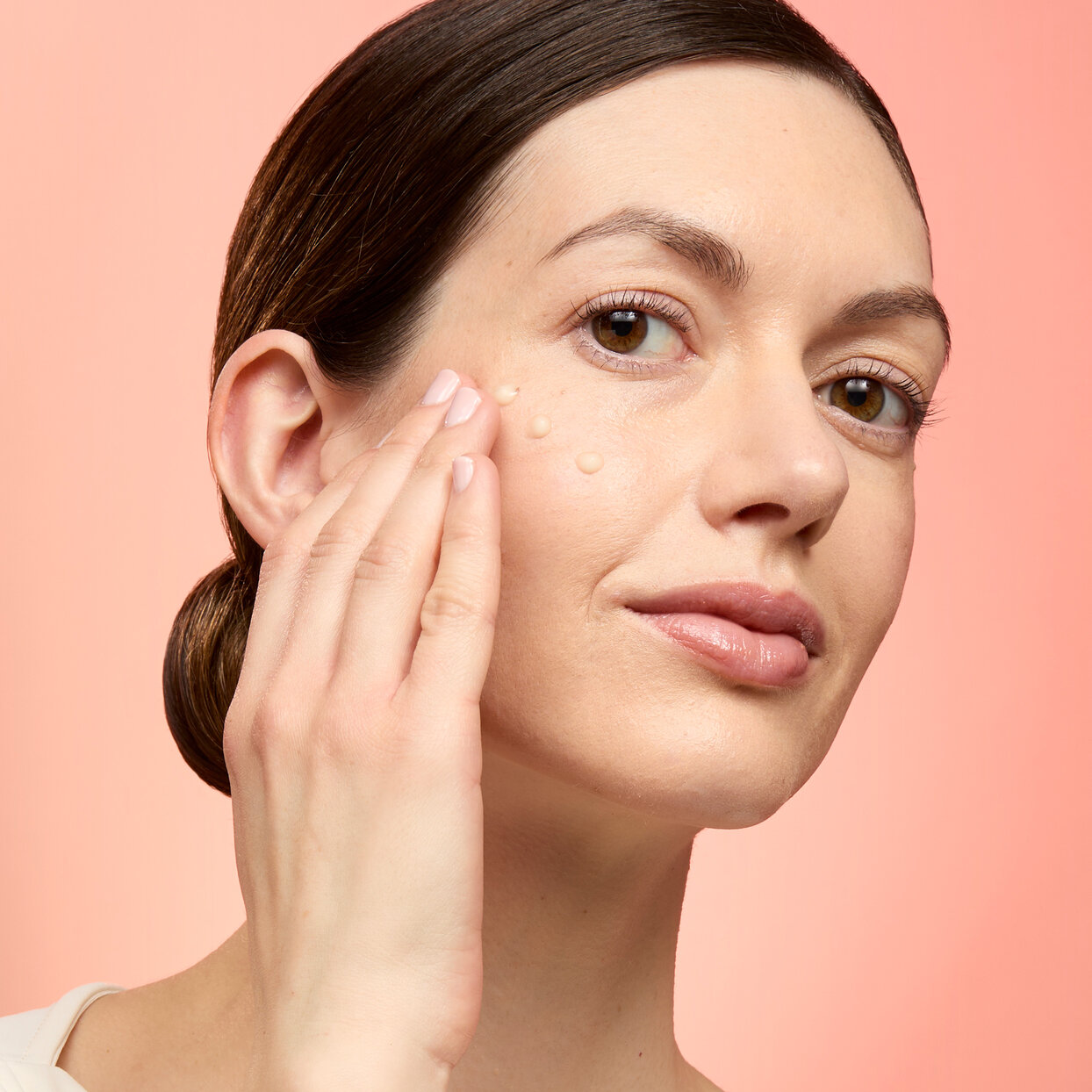 Restore & Glow™ Instant Radiance Serum woman applying a serum to her cheeks with her fingers on a peach background