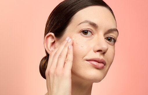 woman applying serum to her face on a peach background